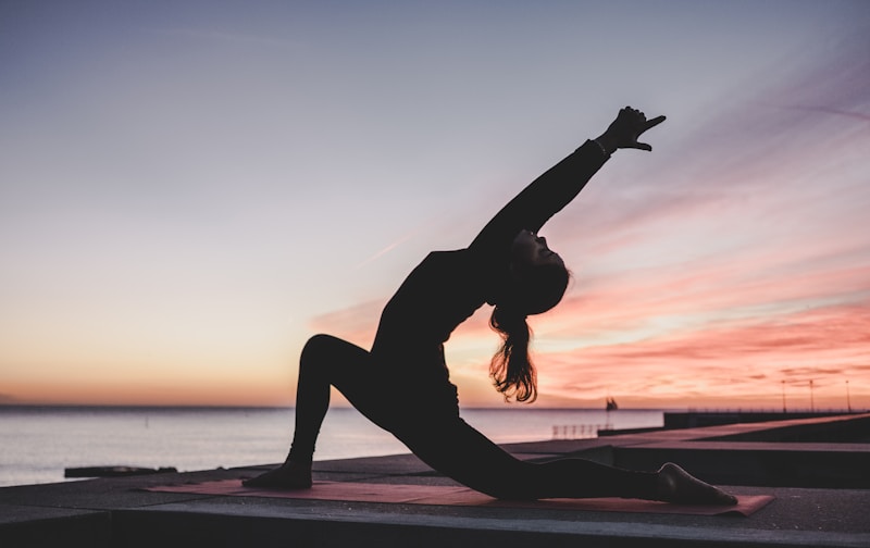 Silhouette of a person in a yoga lunge on a pier at sunset overlooking the ocean